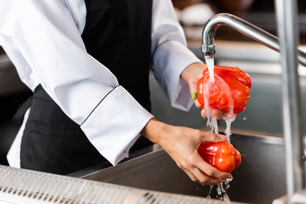 Cropped view of chef washing bell peppers near faucet in kitchen  - Foto, Imagen
