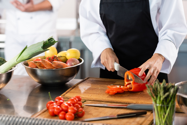 Cropped view of chef cutting bell pepper near knifes and vegetables in kitchen  - Foto, imagen