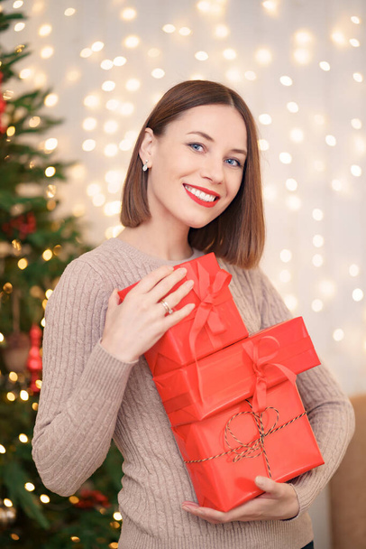 Belle femme brune tenant tas de boîtes-cadeaux dans le salon décoré - Photo, image