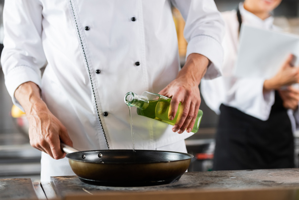 Cropped view of chef pouring olive oil on frying pan on cooktop in kitchen  - Fotografie, Obrázek
