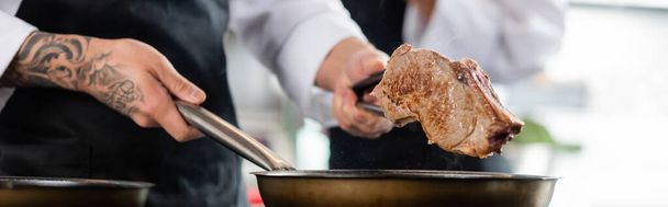 Καλλιεργημένη άποψη του σεφ με λαβίδες που κατέχουν κρέας και τηγάνι στην κουζίνα, πανό  - Φωτογραφία, εικόνα