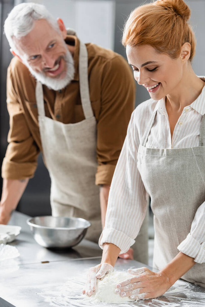Chef haciendo masa cerca borrosa sonriente colega en la cocina  - Foto, Imagen