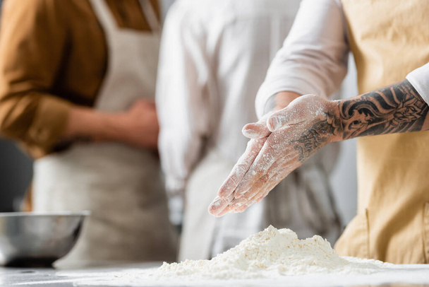 Cropped view of tattooed chef standing near flour on table in kitchen  - Фото, изображение