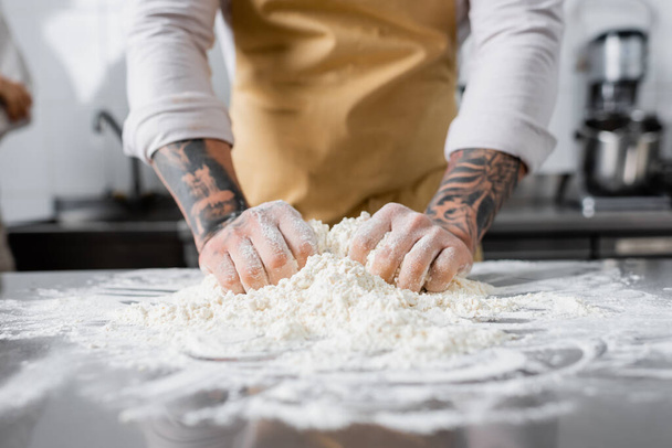 Cropped view of tattooed chef making dough near blurred flour in kitchen  - Foto, Imagem