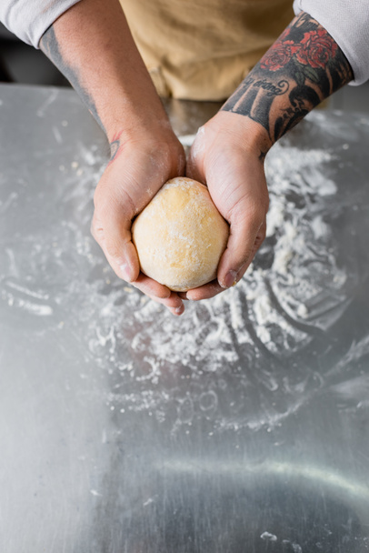 Top view of tattooed chef holding dough near flour on kitchen table  - Foto, immagini