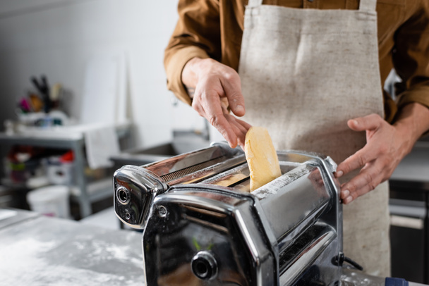 Vista ritagliata dello chef in grembiule mettere pasta in macchina pastificatrice in cucina  - Foto, immagini