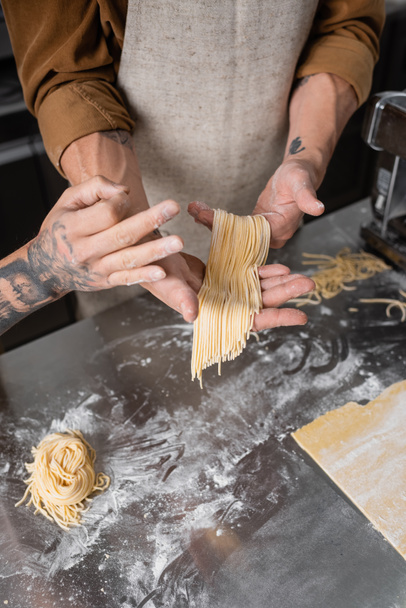 Vista recortada de chef tatuado mostrando gesto ok cerca de colega con espaguetis crudos en la cocina  - Foto, Imagen