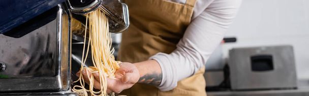 Vue recadrée d'un chef tatoué faisant des spaghettis sur une machine à pâtes dans la cuisine, bannière  - Photo, image