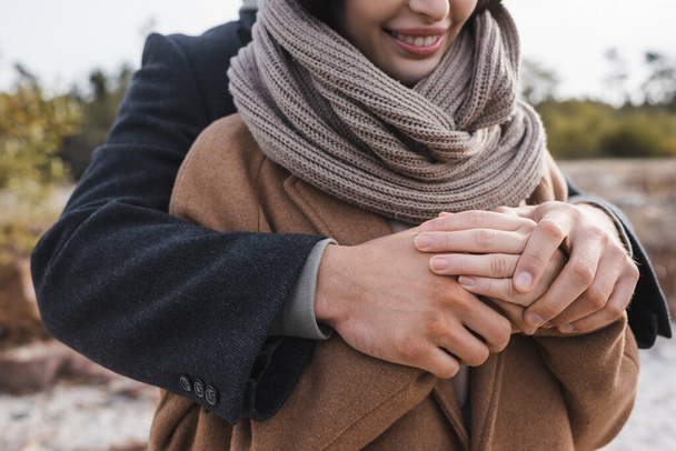 partial view of man hugging smiling woman in autumn coat and scarf outdoors - Photo, Image