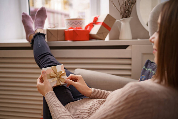 Egy nő ül otthon egy karosszékben, ajándékkal a kezében. - Fotó, kép