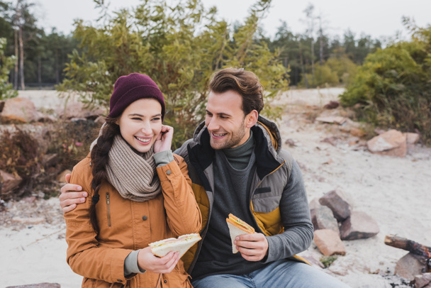 smiling man embracing girlfriend while eating sandwiches during halt - Photo, Image
