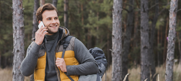 smiling tourist talking on mobile phone while walking in autumn forest, banner - Photo, Image