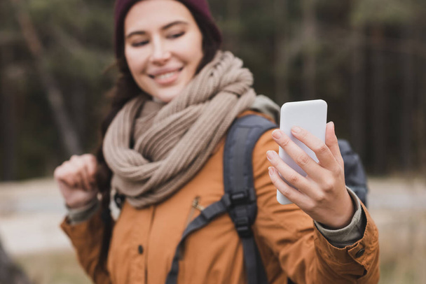 blurred woman smiling while taking selfie on mobile phone outdoors - Photo, Image