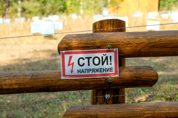Warnung an einem Holzzaun. Russischer Text: Stopp. Spannung. - Foto, Bild