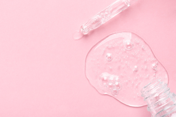 Маленькая бутылка и стеклянная пипетка с прозрачным гелем на светло-розовый - Фото, изображение