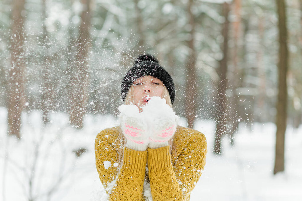Piękna młoda dziewczyna ciesząca się zimą na zewnątrz. Ładne kobiety bawiące się śniegiem w lesie lub parku. blondynka wieje śnieg - Zdjęcie, obraz