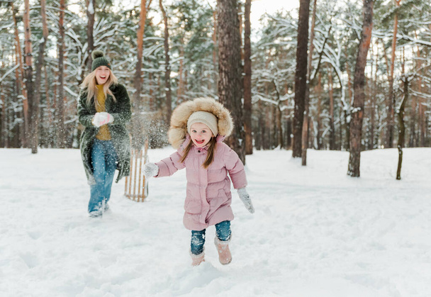 Happy and smilling young mother and her little daughter having fun outside, in winter park - 写真・画像