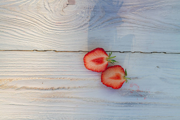 A strawberry berry cut in half on a white wooden background. - Zdjęcie, obraz