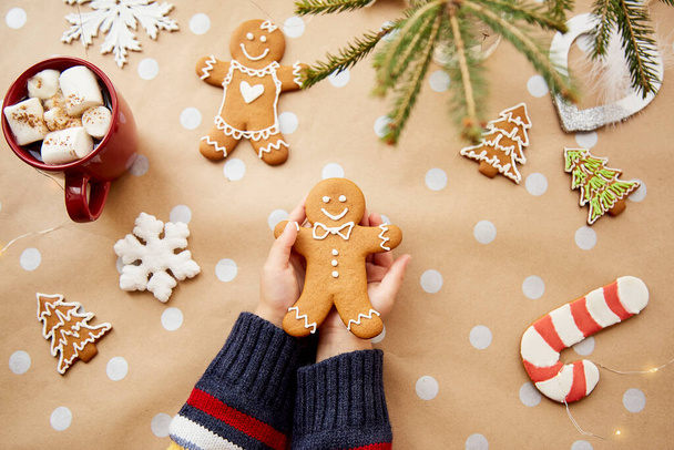 Dítě drží vánoční domácí perníkové sušenky mezi slavnostními vánočními ozdobami s teplým nápojem a bažinami. Slavnostní vánoční atmosféra, domácí útulnost a vřelost koncept - Fotografie, Obrázek