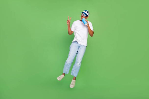 Full size photo of cool millennial brunet guy drink beverage jump wear white t-shirt jeans shoes isolated on green background. - Fotoğraf, Görsel