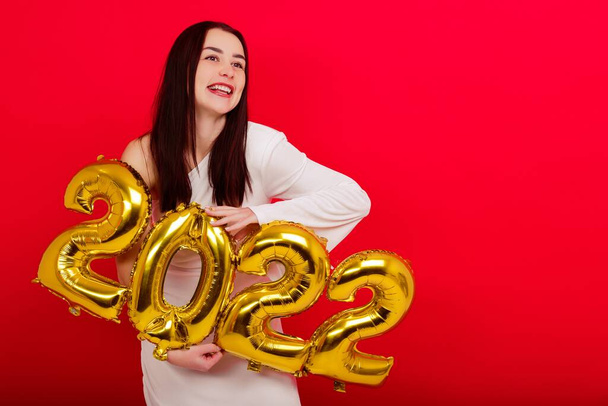 Joululoma - Nuori nainen valkoisessa mekossa pitää numeroita 2022 punaisella taustalla - Valokuva, kuva