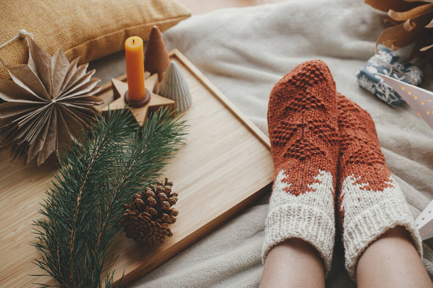 Woman legs in warm socks on soft blanket with christmas star, trees and candle. Cozy moments at home. Winter and autumn holidays. Girl  relaxing on bed with pillows and festive holiday decoration - Zdjęcie, obraz