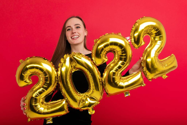 A happy brunette in a black dress holds the numbers 2022 on a red background - Fotoğraf, Görsel