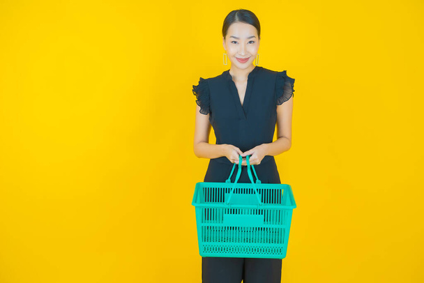 Portrét krásná mladá asijská žena úsměv s nákupním košíkem ze supermarketu na barevném pozadí - Fotografie, Obrázek