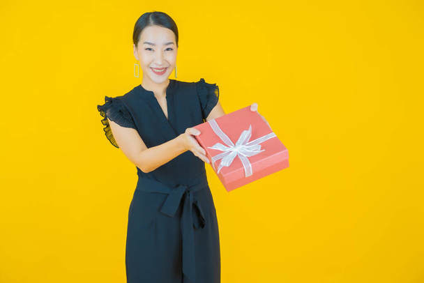 Porträt schöne junge asiatische Frau lächeln mit rotem Geschenkkarton auf farbigem Hintergrund - Foto, Bild