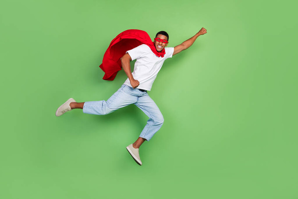 Full length profile photo of impressed super man brunet guy fly wear courage mask t-shirt jeans footwear isolated on green background. - 写真・画像