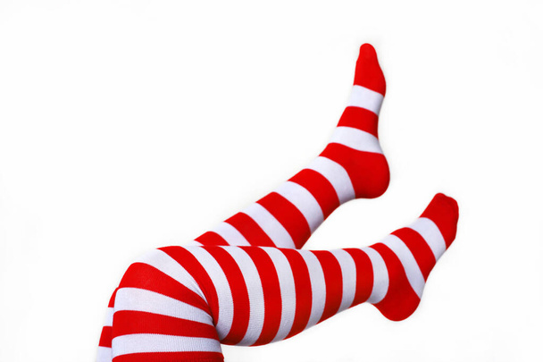 Female legs in Christmas knee socks on white background. Concept of New Year celebration, girl in stockings with red and white stripes - Photo, Image