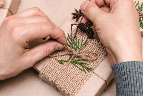 Cristmas decoration of gifts in eco-style,male hands close-up,top view.Gift boxes are wrapped in craft paper,decorated with thuja leaves and cones.Christmas,New Year and eco-friendly concept. - Foto, Imagem