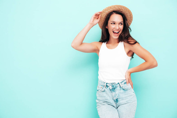 Young beautiful smiling female in trendy summer  clothes. Sexy carefree woman posing near blue wall in studio. Positive brunette model having fun. Cheerful and happy. In hat - Φωτογραφία, εικόνα