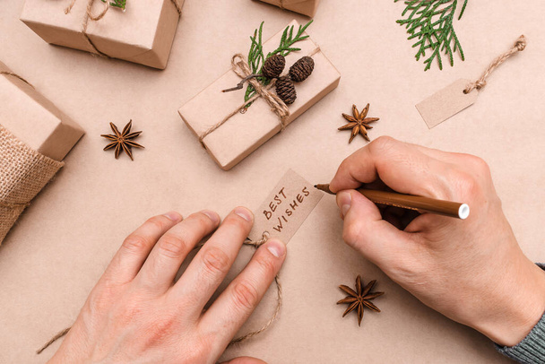 Christmas decoration of gifts in eco-style,male hands close-up,top view.Gift boxes are wrapped in craft paper,decorated with thuja leaves and cones.Christmas,New Year and eco-friendly concept. - Foto, Bild
