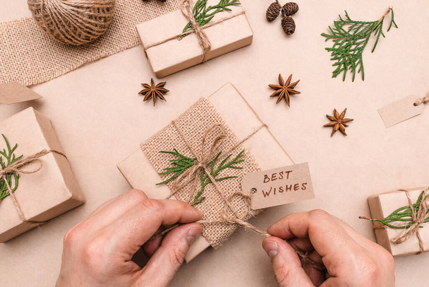 Festive decoration of gifts in eco-style,male hands close-up,top view.Gift boxes are wrapped in craft paper,decorated with thuja leaves and cones.Christmas,New Year and eco-friendly concept. - Foto, Bild