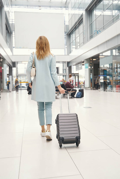 Female passenger pulling luggage along airport terminal - Photo, image