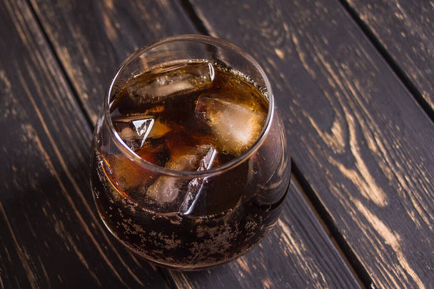 Beautiful glass with whiskey cola and ice on a dark brown wooden table background. Delicious and elegant gossed alcoholic cocktail at the bar. - Zdjęcie, obraz