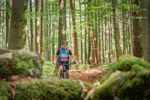 mulher sênior bonita em andamento em sua bicicleta de montanha elétrica em uma trilha de floresta rochosa na Suíça Franconiana, Baviera, Alemanha - Foto, Imagem