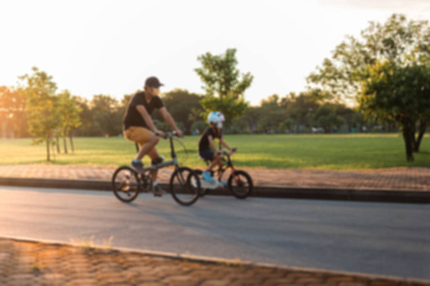 Padre e hijo montando bicicletas en el parque al atardecer. - Foto, imagen