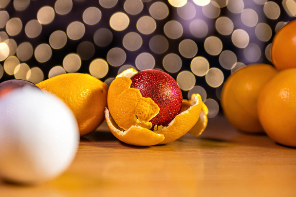 table with oranges and Christmas balls on a background of bokeh lights, xmas ball in orange peel - Photo, image