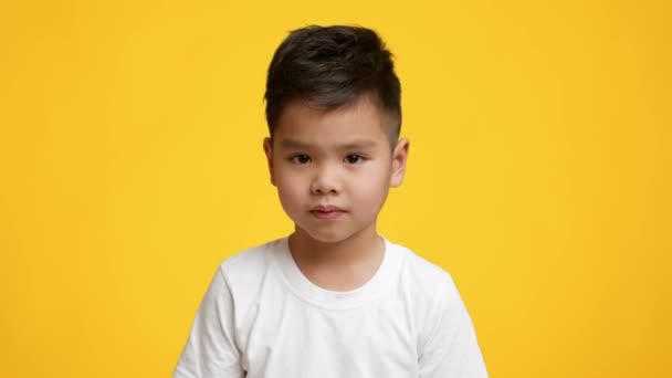 黄色の背景の上にポーズを取る無慈悲な韓国の小さな男の子の肩を振る - 映像、動画