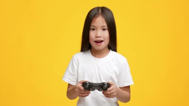 Menina asiática jogando jogo de vídeo se divertindo sobre fundo amarelo - Filmagem, Vídeo