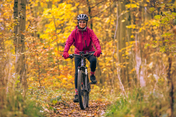 シュトゥットガルト近くの秋の森の小道をマウンテンバイクに乗っている素敵な先輩女性、美しい暖かい色、バーデン=ヴュルテンベルク州、ドイツ - 写真・画像