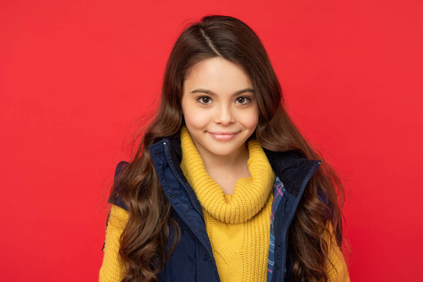 smiling child with curly hair in winter down vest on red background, hair - Foto, afbeelding