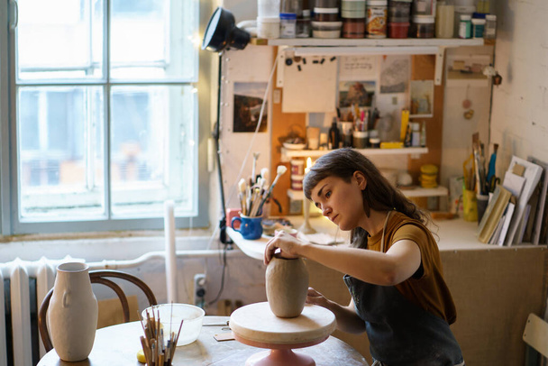 Talented female ceramist shaping vase in studio. Artistic workshop owner woman busy with pottery - Foto, imagen