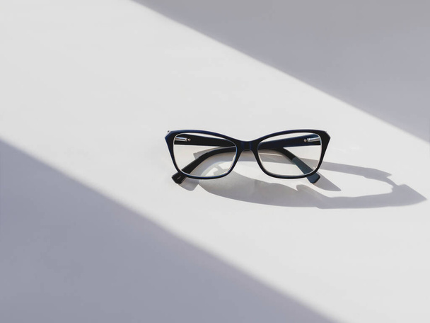 Top view of eyeglasses on white background. Comfortable life with poor eyesight. Ophthalmology. Contrast of hard sunlight and geometrical shadow. - Foto, imagen