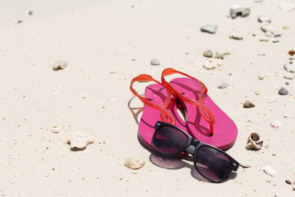 Μαύρα γυαλιά ηλίου και ροζ παπούτσια στην παραλία της θάλασσας το καλοκαίρι. - Φωτογραφία, εικόνα