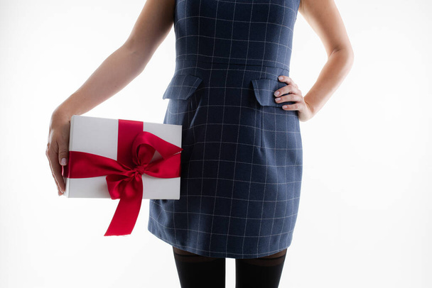 Jonge vrouw in een jurk en panty houdt een geschenk in een doos - Foto, afbeelding