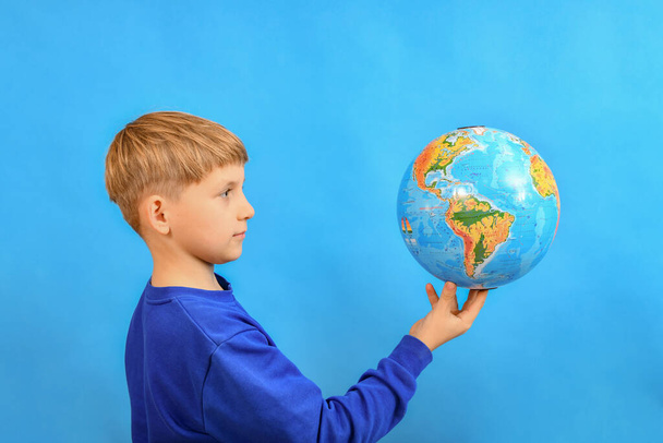 The boy holds the globe on his index finger and looks at it. - Fotoğraf, Görsel