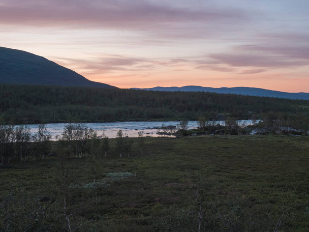 Puesta de sol de color rosa anaranjado en el agua salvaje de los rápidos del río Vuojatadno, la montaña y el bosque de abedules. Hermoso paisaje ártico del norte en Laponia sueca. Tarde de verano en el sendero Padjelantaleden. - Foto, imagen